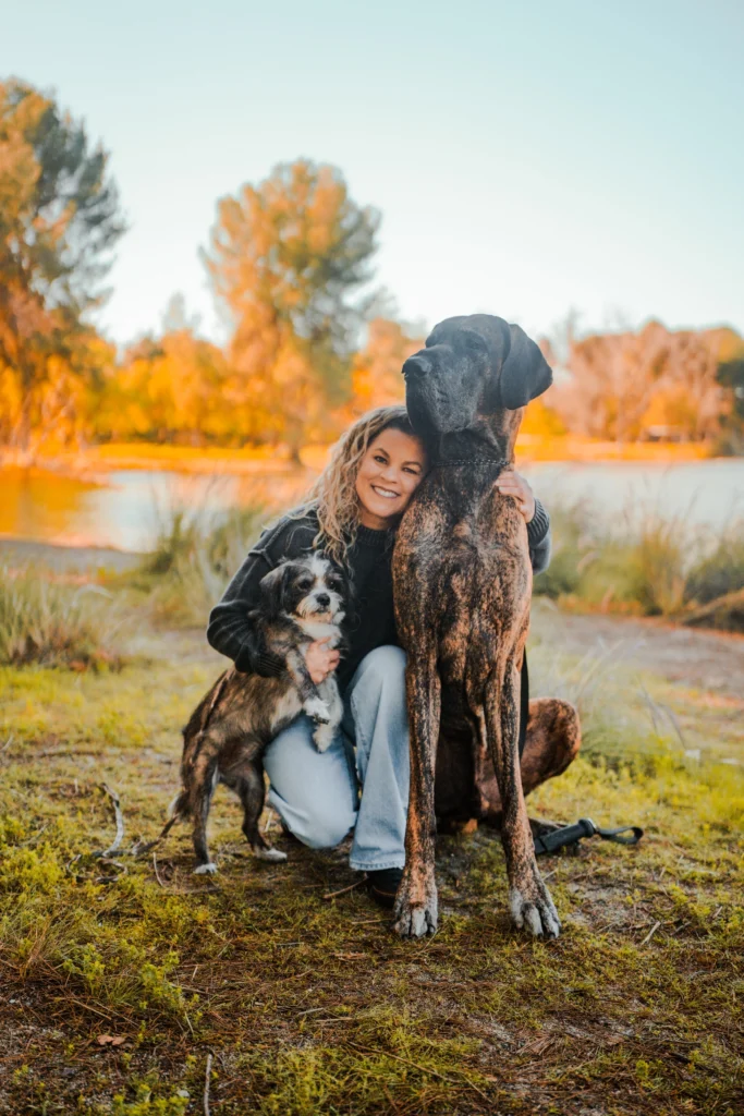 Fullerton therapist Keri Prather, LMFT, smiling outdoors with her supportive office dogs, Piper and Anders.